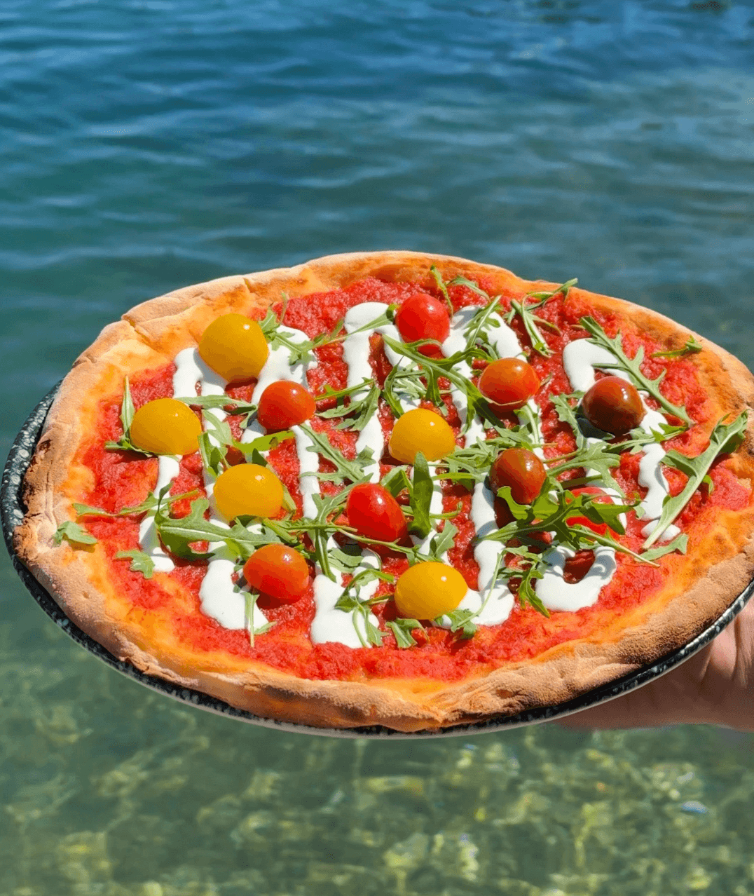 Wood-fired pizza with cherry tomatoes and arugula held over Zaton bay at Dandy, near Dubrovnik